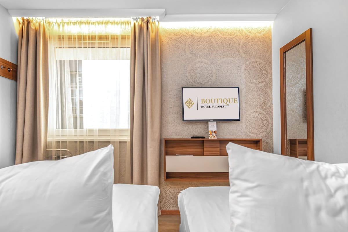 A hotel room with a bed, a TV on the wall, and a window with curtains.