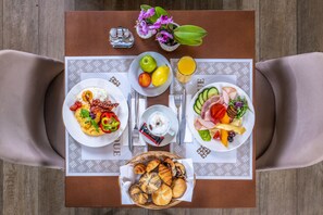 A breakfast table with plates of food, a basket of croissants, a fruit bowl, and a glass of orange juice. - Charm Hotel Budapest  (formerly Boutique Hotel Budapest) (Budapest)