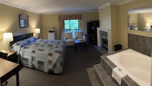 A hotel room with a large bed, a sitting area with a chair and a table, a bathroom with a bathtub, and a fireplace. - Canadian Inn (Surrey)