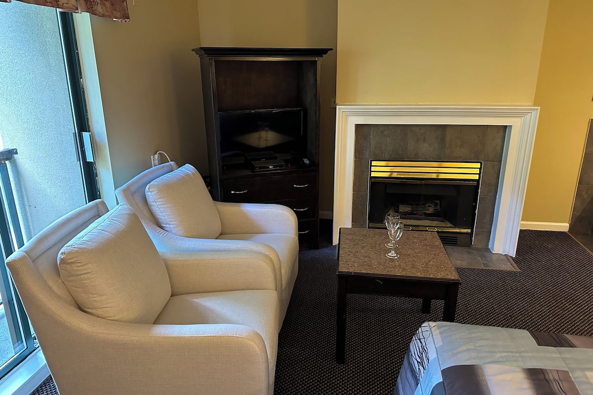 A hotel room with a beige sofa, a small table with a glass, and a fireplace.