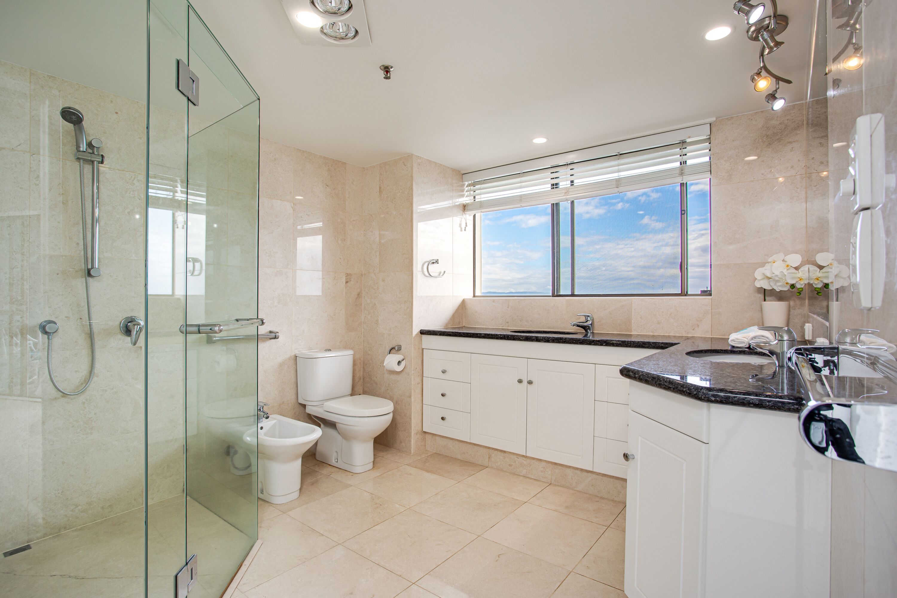 A modern bathroom with a glass shower enclosure, a toilet, a bidet, and a sink with a vanity.