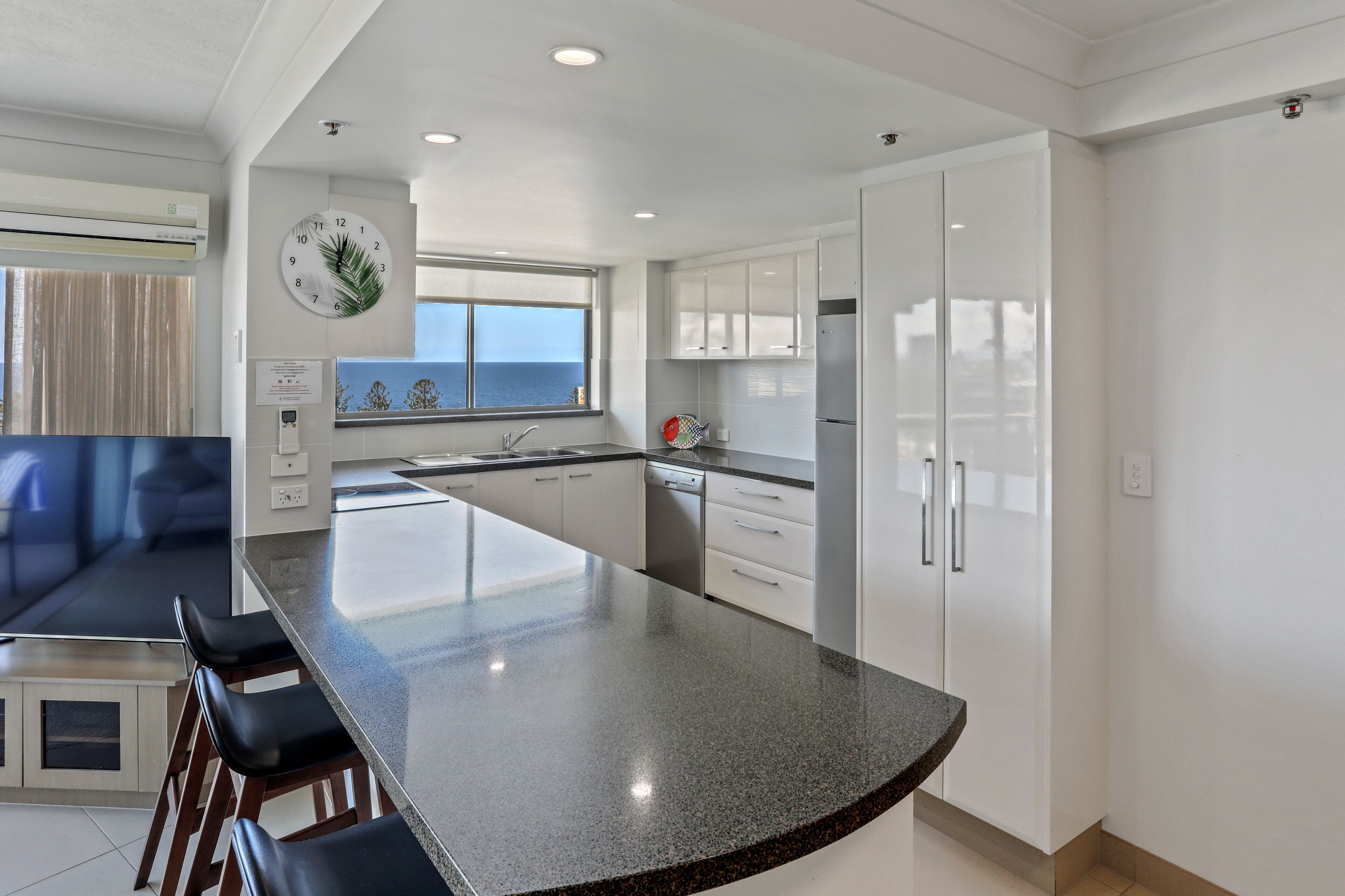 A modern kitchen with a large island, white cabinets, and a view of the sea.