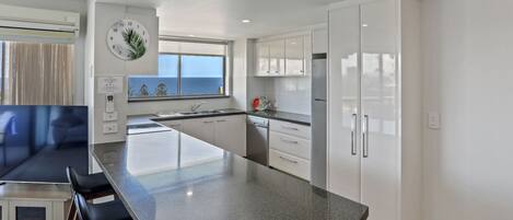 A modern kitchen with a large island, white cabinets, and a view of the sea.