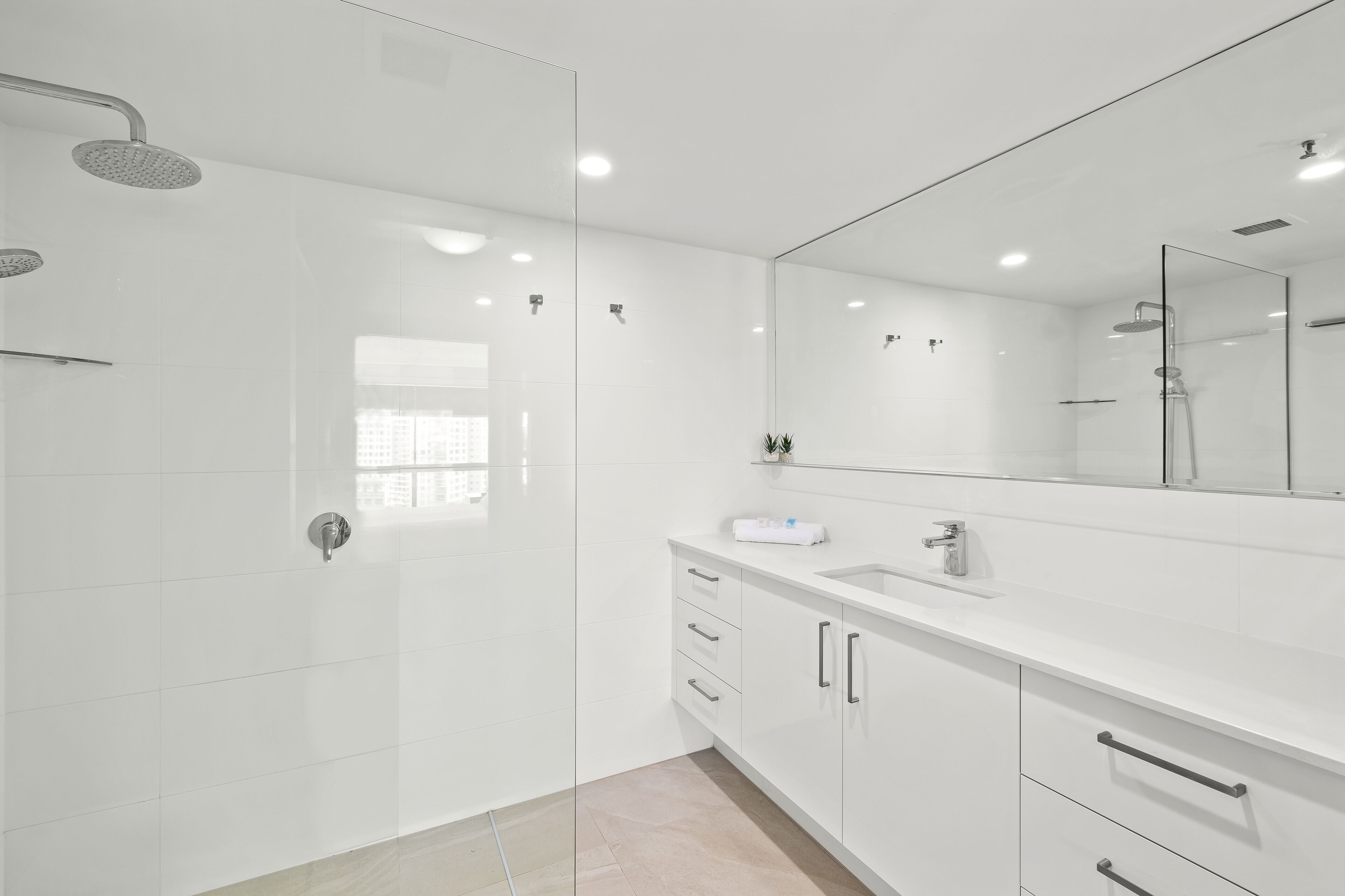 A modern bathroom with a glass shower enclosure, a large mirror, and a white vanity with drawers.