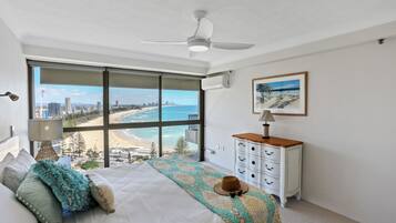 Un dormitorio con un ventanal que ofrece vistas a la playa y al paisaje urbano.