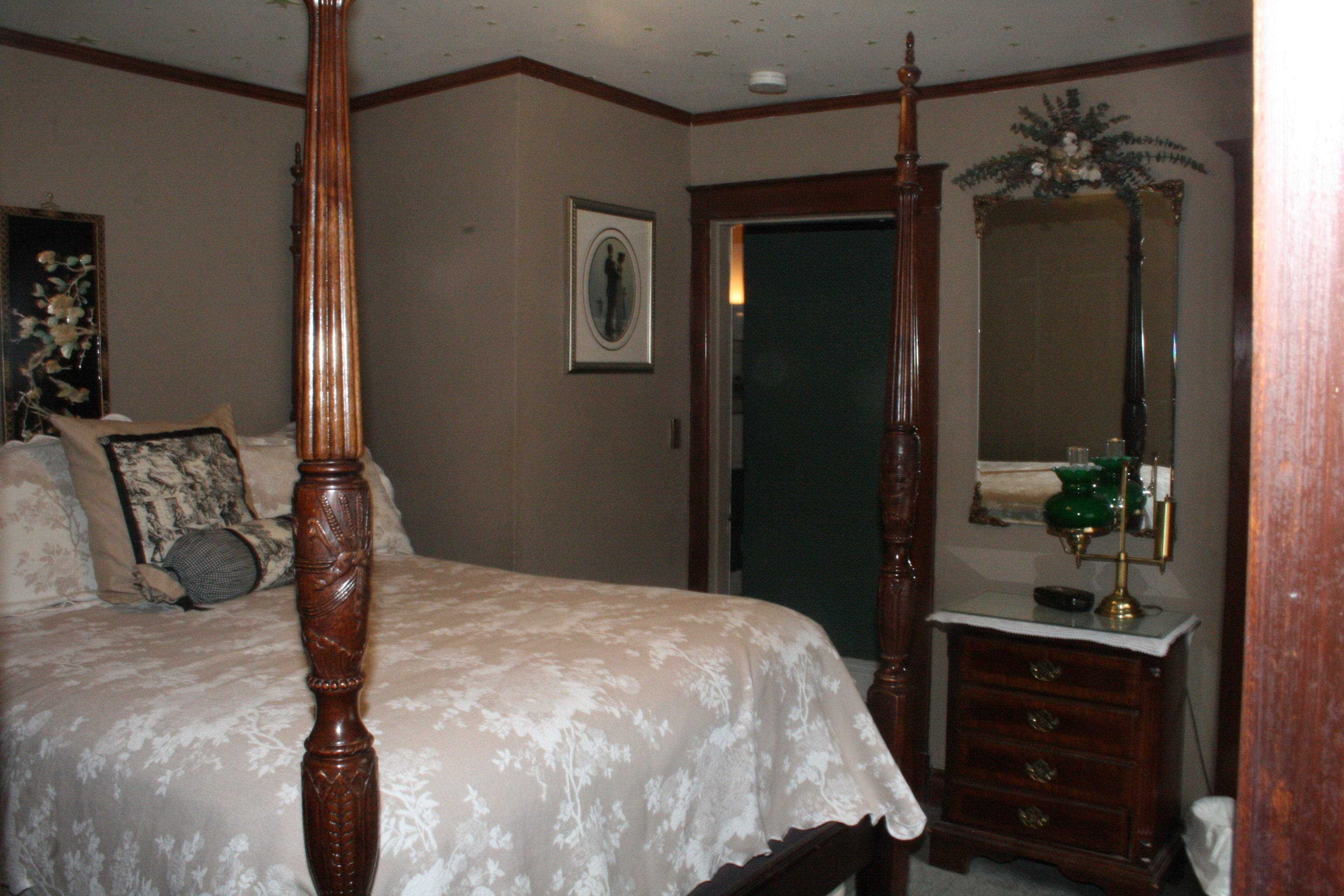 A bedroom with a four-poster bed, a dresser, and a mirror.