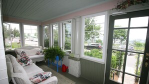 A covered porch with wicker furniture, large windows, and a view of the parking lot. - Rose Arden Bed & Breakfast (Hamilton)