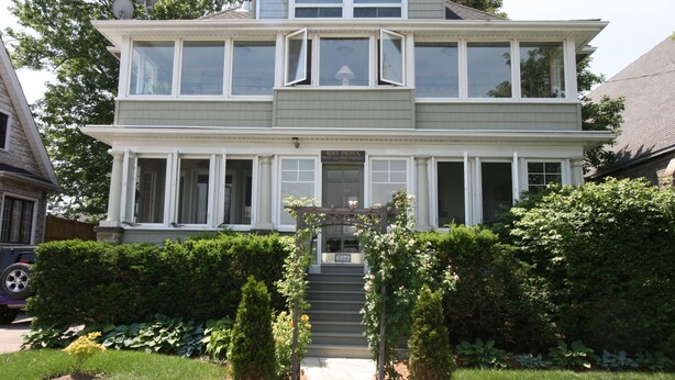 A two-story house with a front porch, a staircase leading to the entrance, and a garden with a small tree and bushes. - Rose Arden Bed & Breakfast (Hamilton)