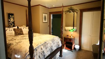 Un dormitorio con cama con dosel, una mesita de noche con lámpara, un cuadro enmarcado en la pared y una puerta que conduce a otra habitación.