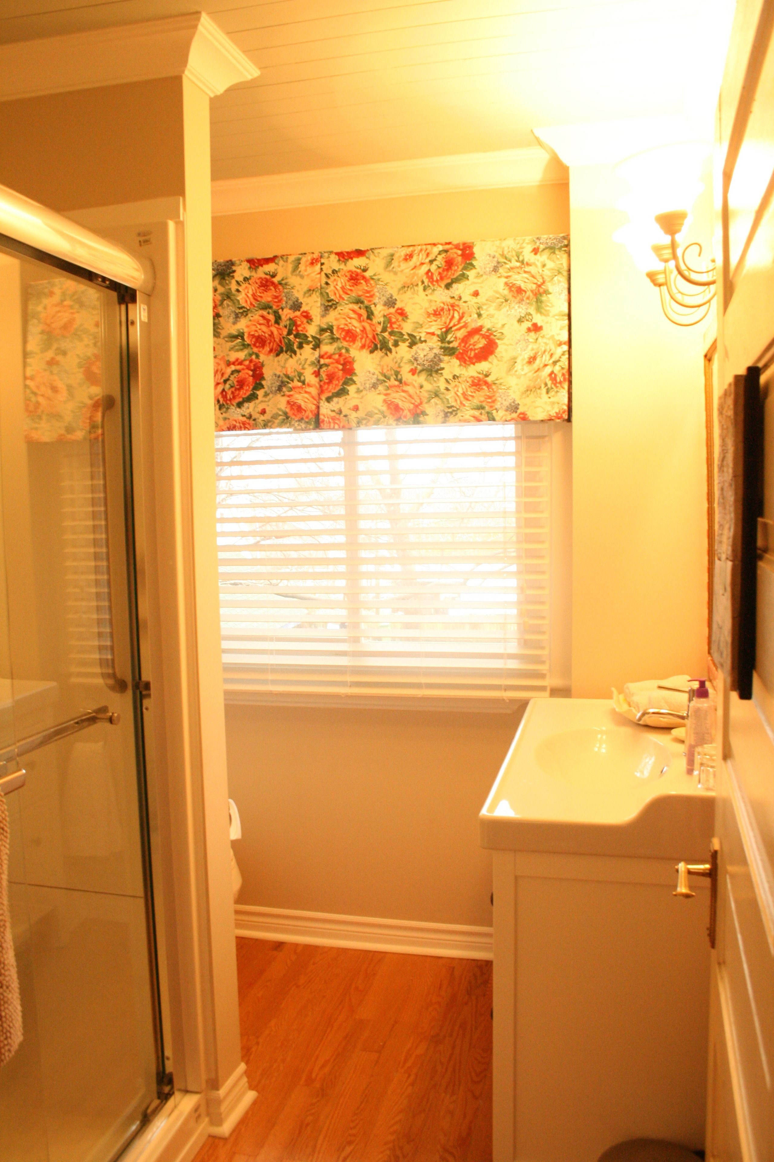 A bathroom with a shower, a sink, and a window with blinds.