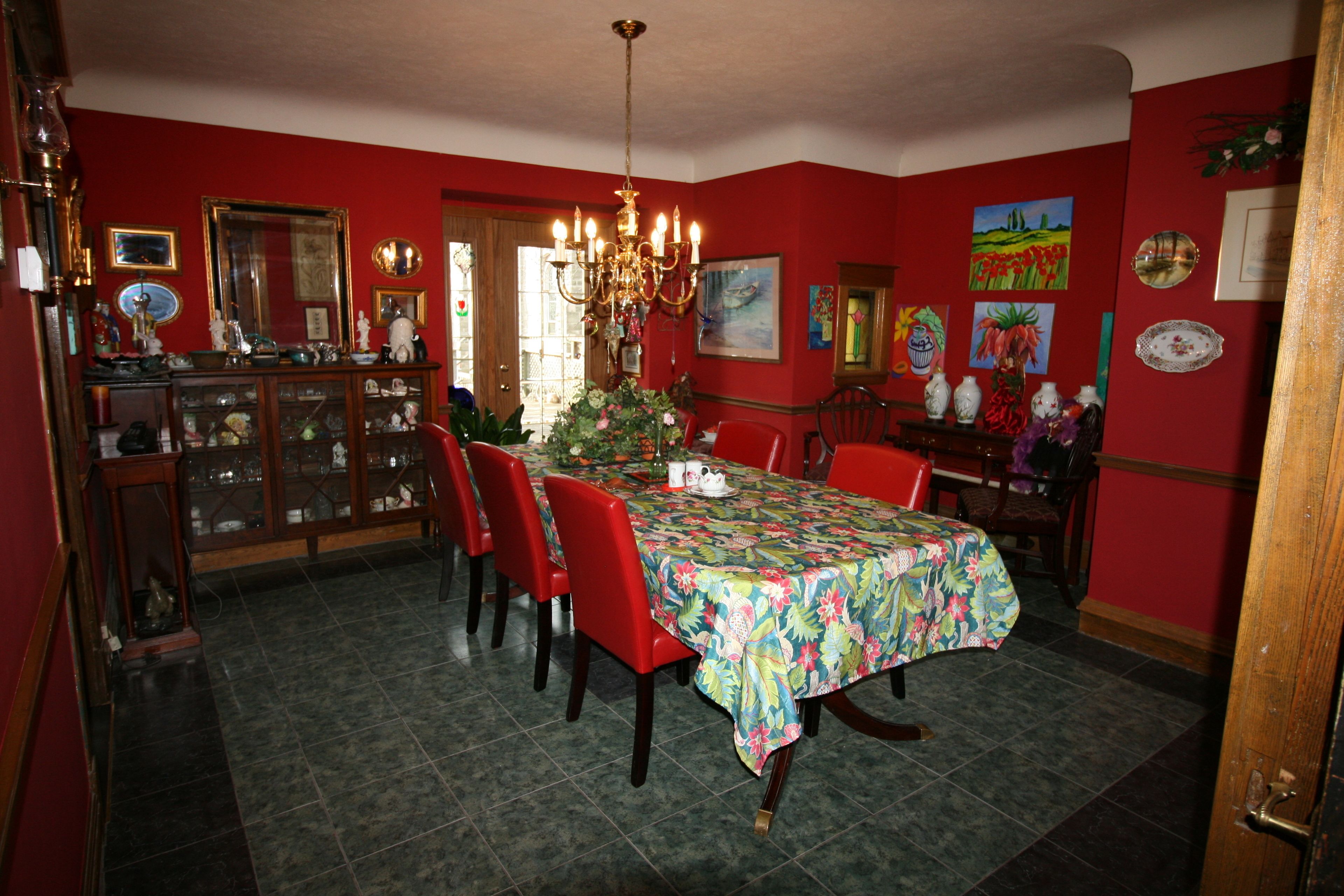 Comedor con pared roja, una lámpara de araña y una mesa cubierta con mantel floreado.