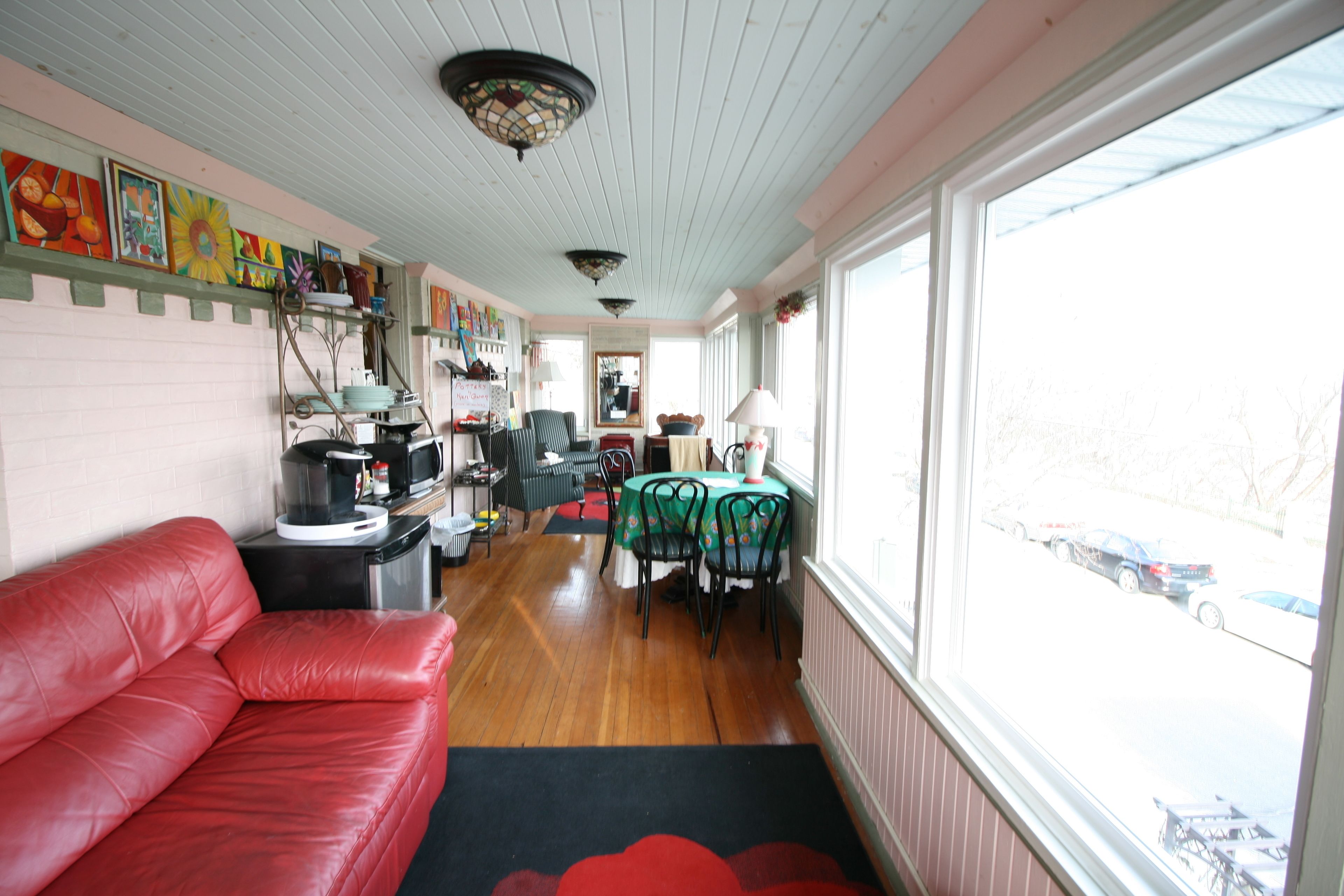 A cozy living room with a red leather couch, a dining area with a table and chairs, and a large window overlooking a parking lot.