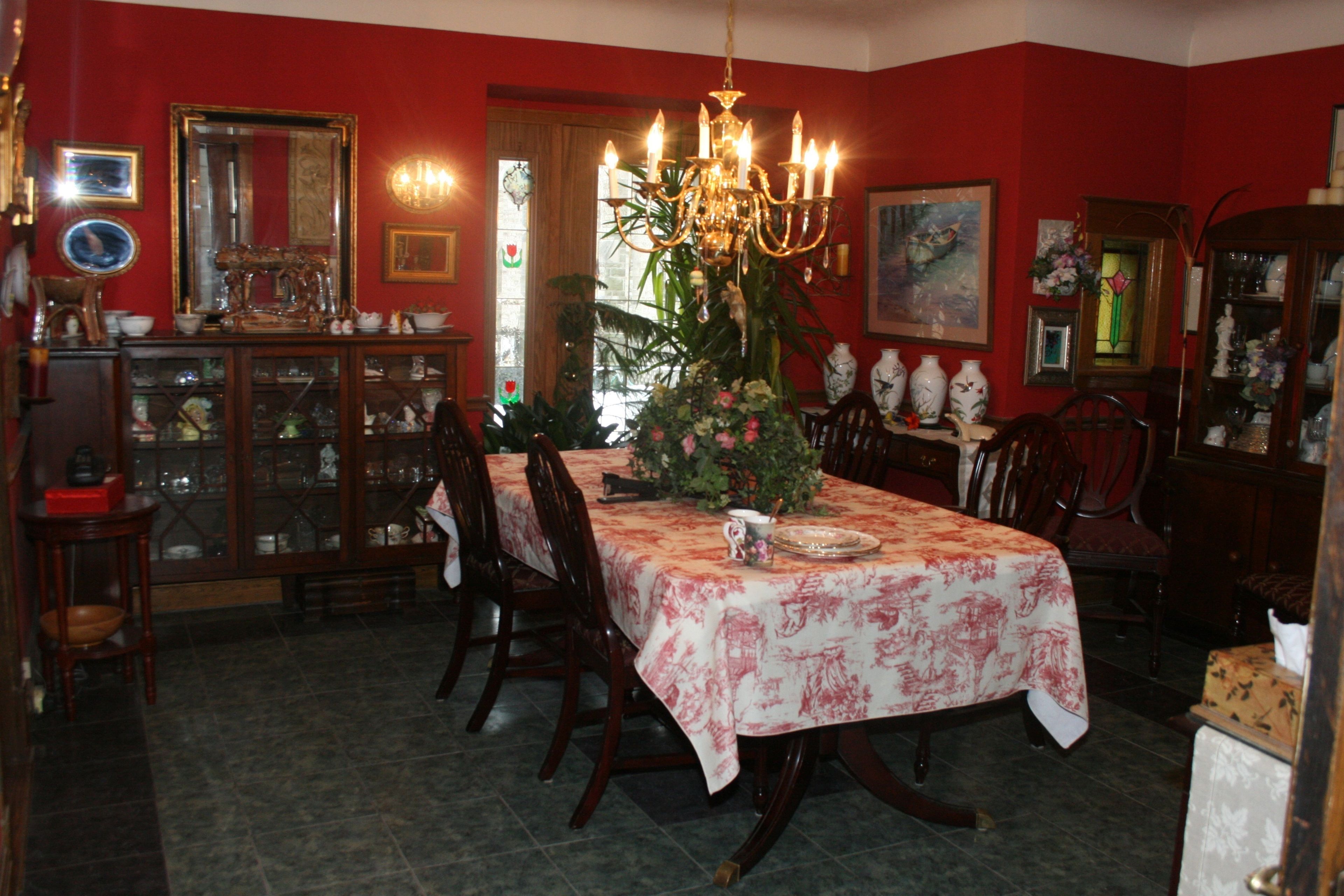 Comedor con una mesa dispuesta para cuatro personas, rodeada de sillas de madera. Un candelabro cuelga sobre la mesa y hay una planta en maceta en el centro.