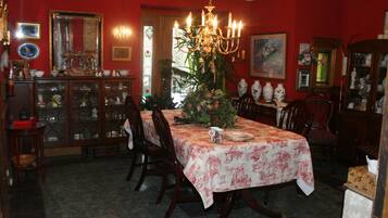 Comedor con una mesa dispuesta para cuatro personas, rodeada de sillas de madera. Un candelabro cuelga sobre la mesa y hay una planta en maceta en el centro.