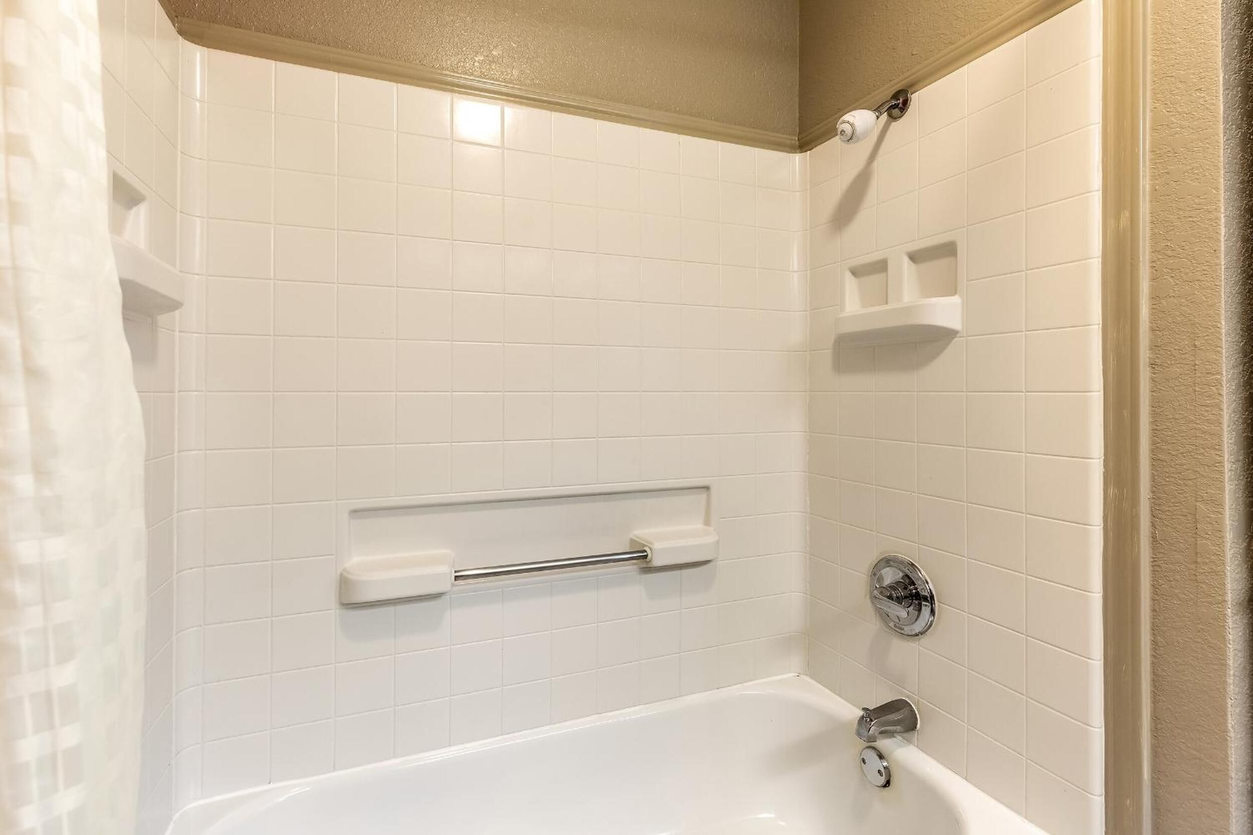 A bathroom with white tiled walls, a bathtub, a towel rack, and a shower curtain.