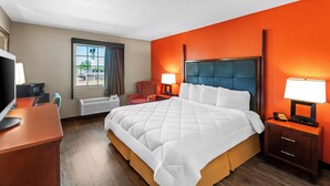 A hotel room with a large bed, a desk with a computer, a chair, a window with curtains, and a nightstand with a lamp. - Rodeway Inn (Temple)