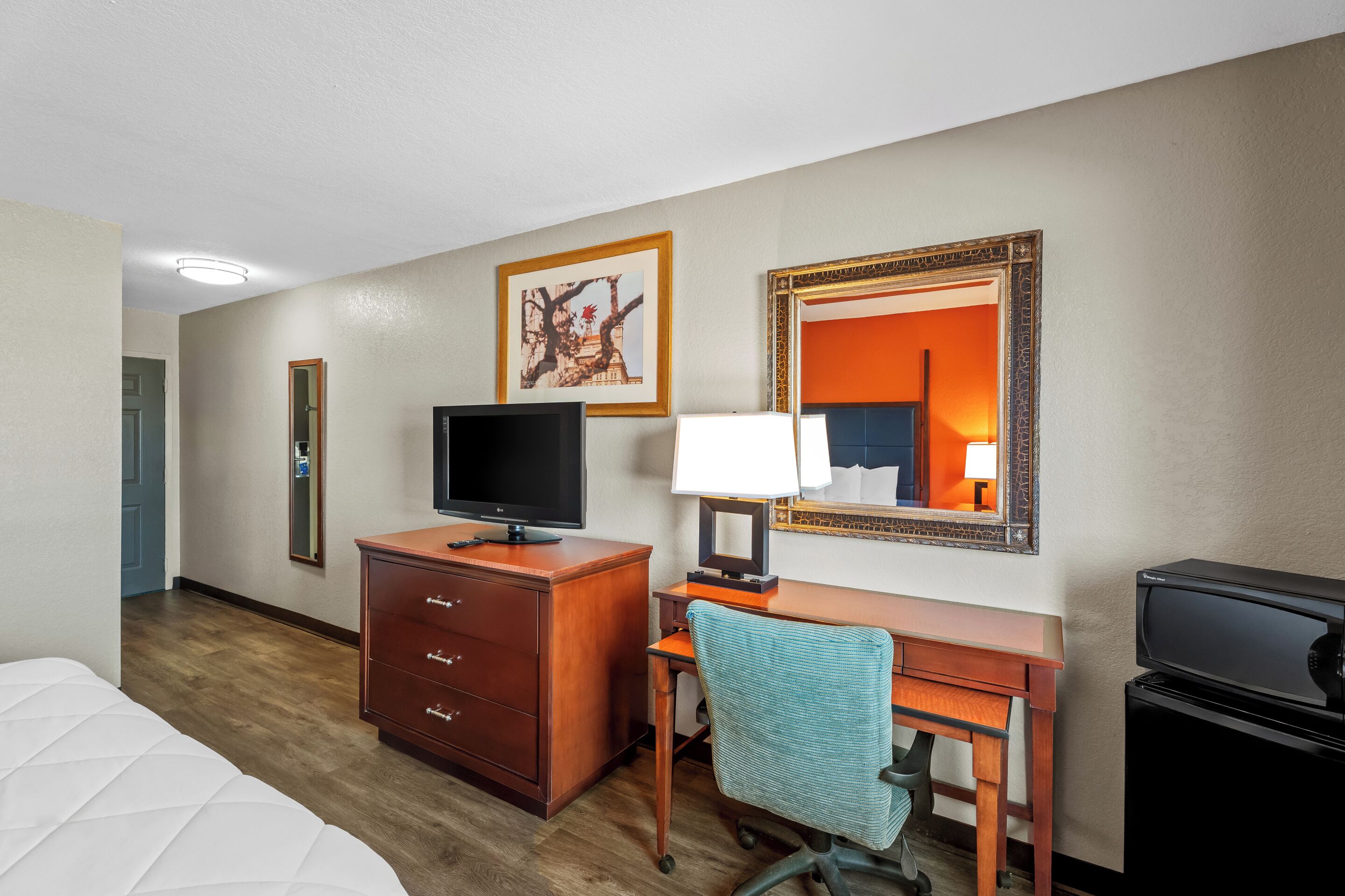 Une chambre d’hôtel comprenant un lit, un bureau avec un ordinateur, une télévision, une lampe et un miroir.