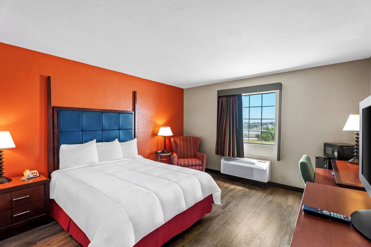 A hotel room with a large bed, a desk, a chair, a TV, and a window with a view.
