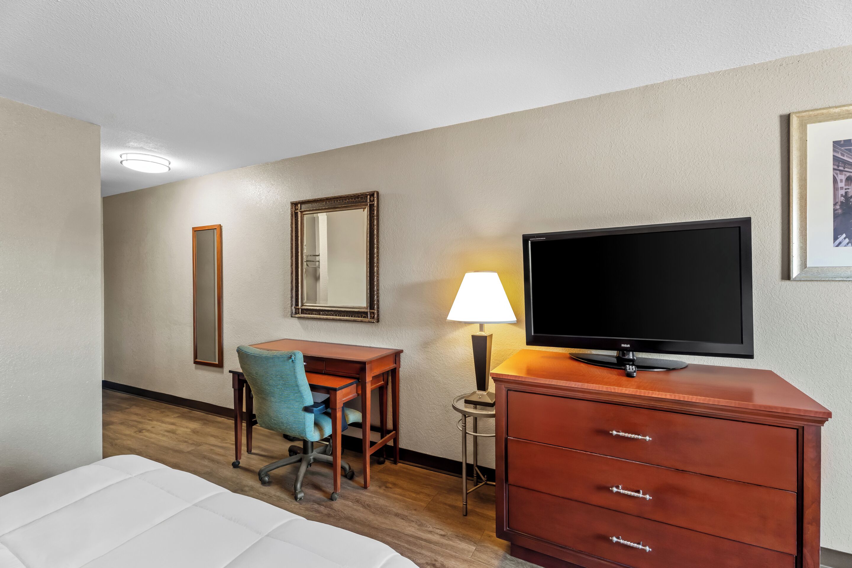 Een hotelkamer met een bed, een bureau, een stoel, een televisie, een lamp en een dressoir.
