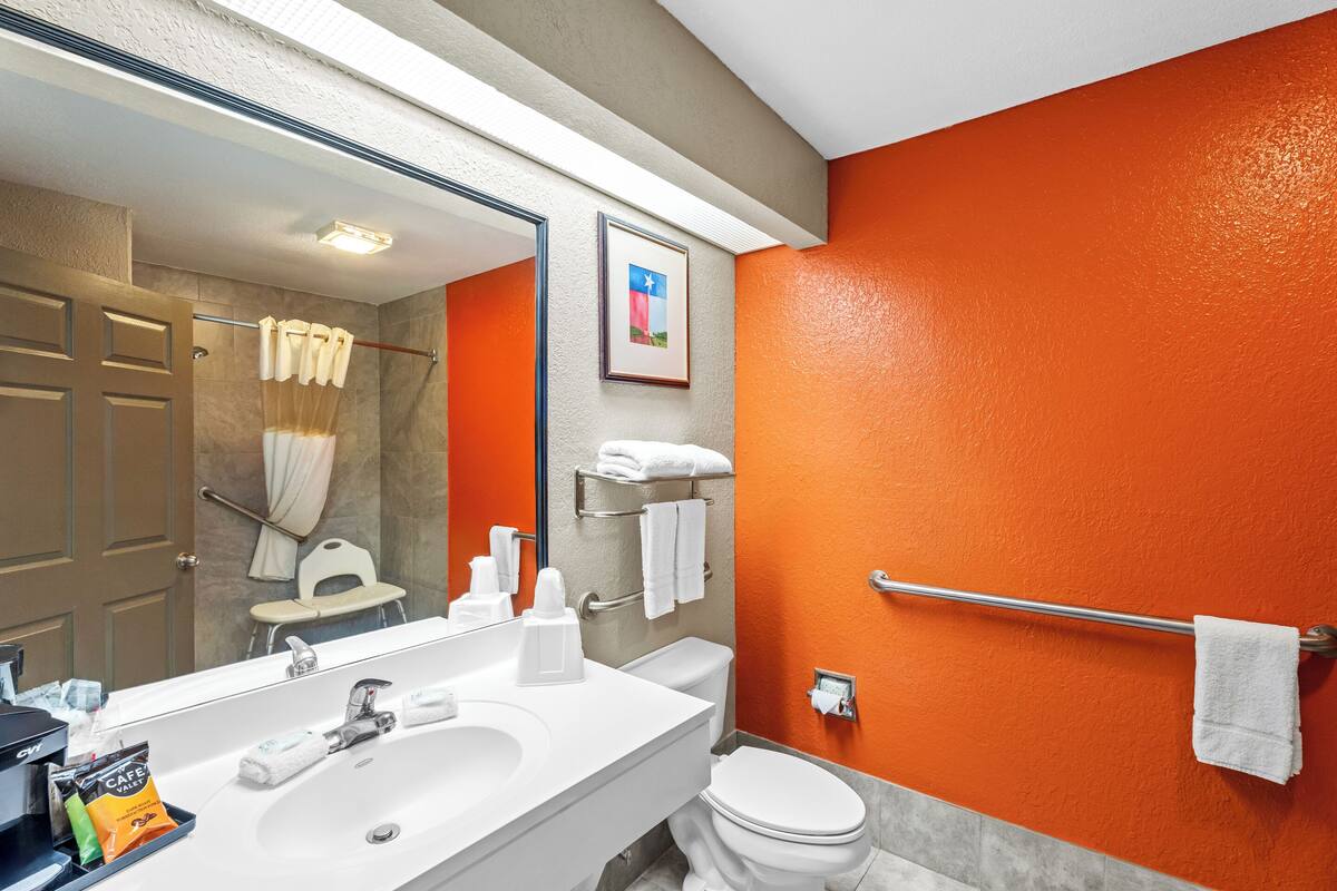 A bathroom with a white sink, mirror, and toilet. There is a towel rack with towels and a framed picture on the wall.
