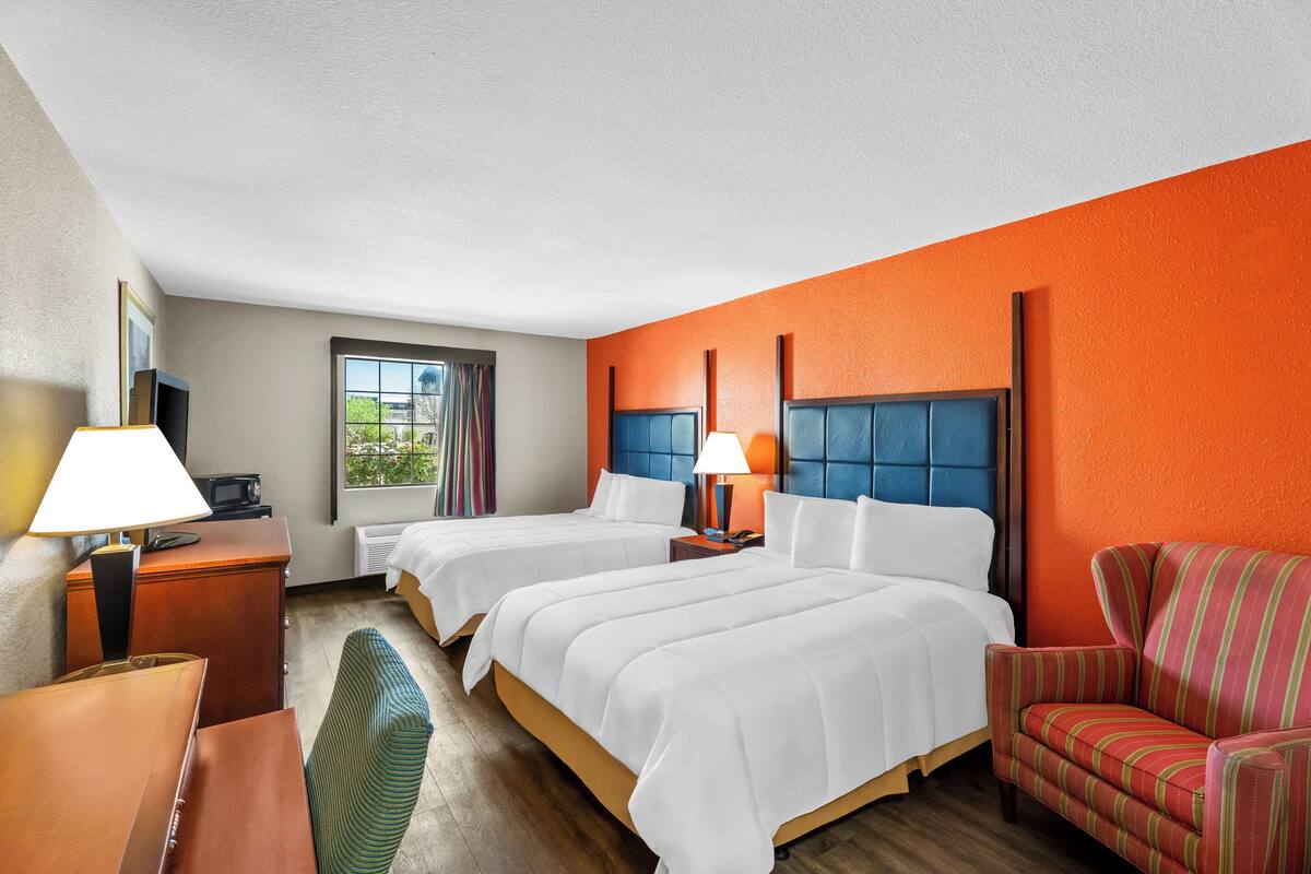 A hotel room with two beds, a desk, a chair, and a window with curtains.