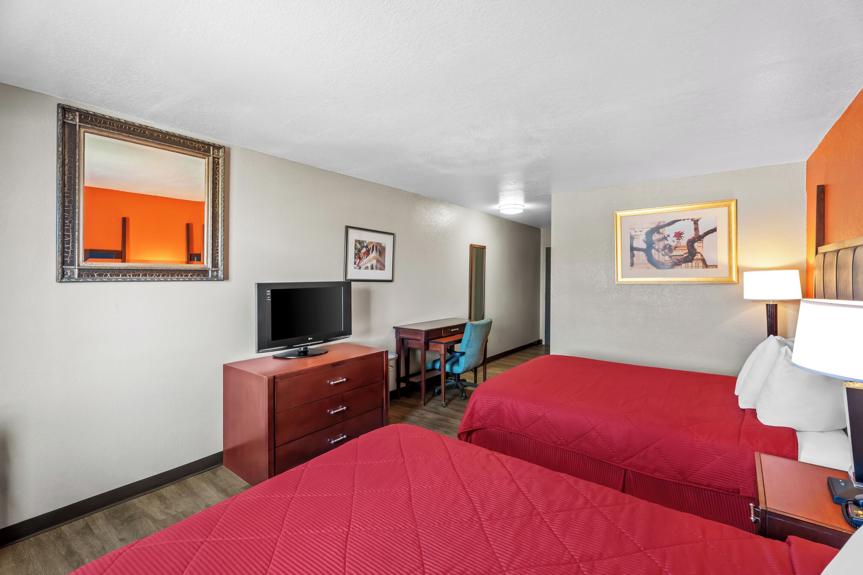 A hotel room with two beds, a desk, a television, and a mirror.