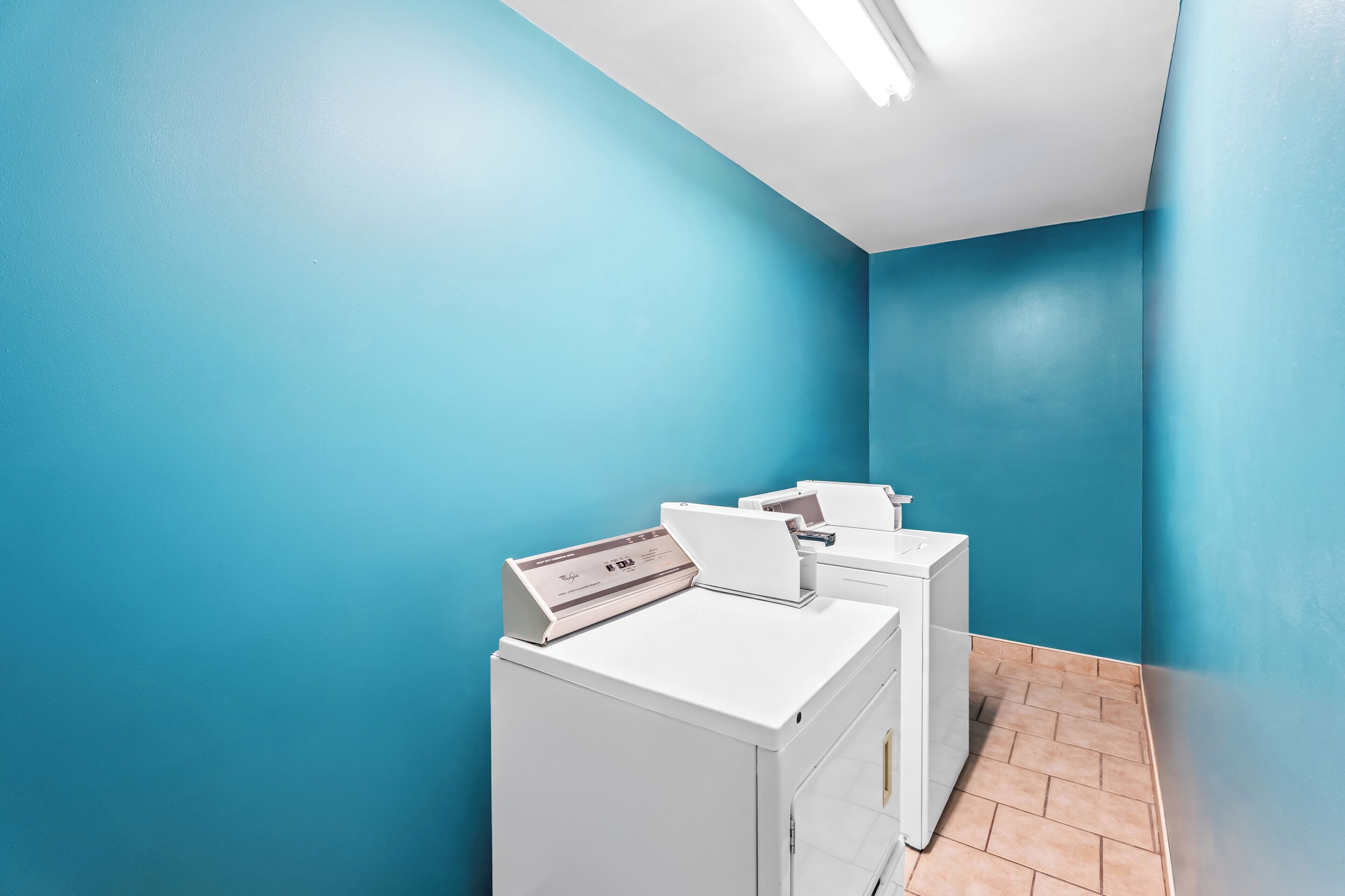 Un cuarto de lavandería con paredes azules y piso de baldosas, que incluye dos lavadoras blancas y una secadora.