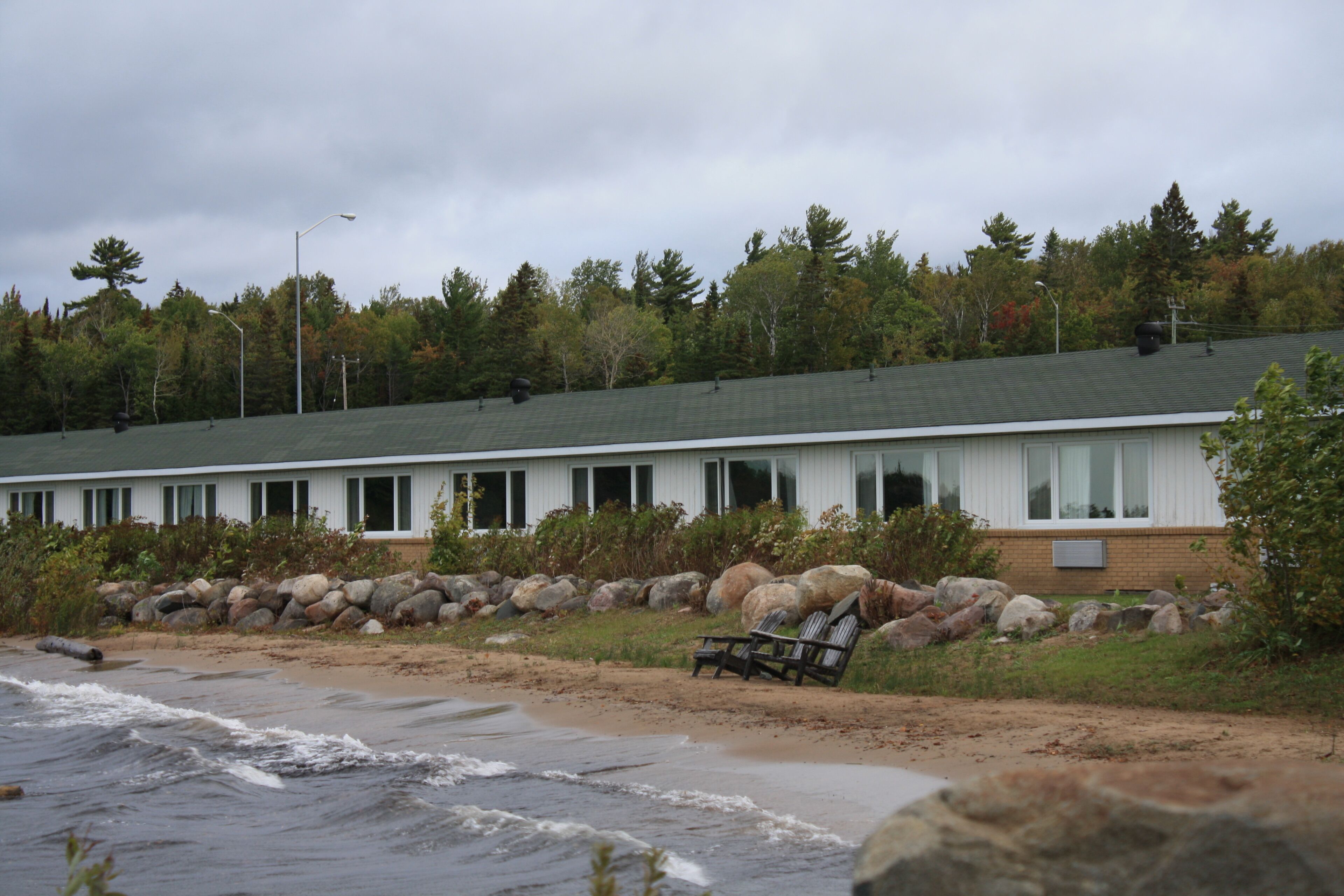 A coastal building with a beach view, large rocks, and a chair by the shore.