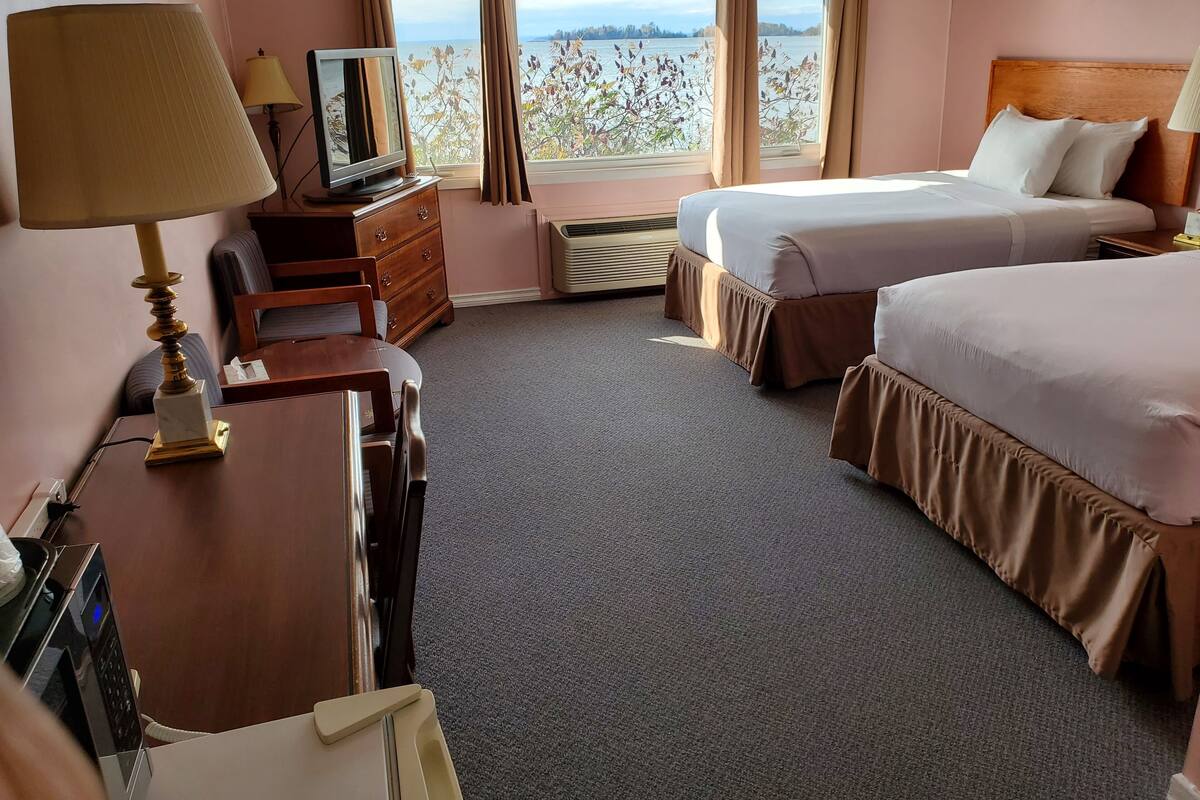 A hotel room with a bed, a desk with a lamp, a television, and a view of the water.