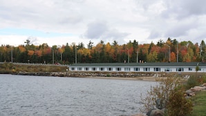 Un edificio a la orilla de un lago con un muelle, rodeado de árboles de colores otoñales.
