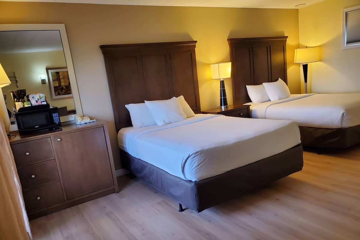 A hotel room with two beds, a dresser, a microwave, and a lamp.