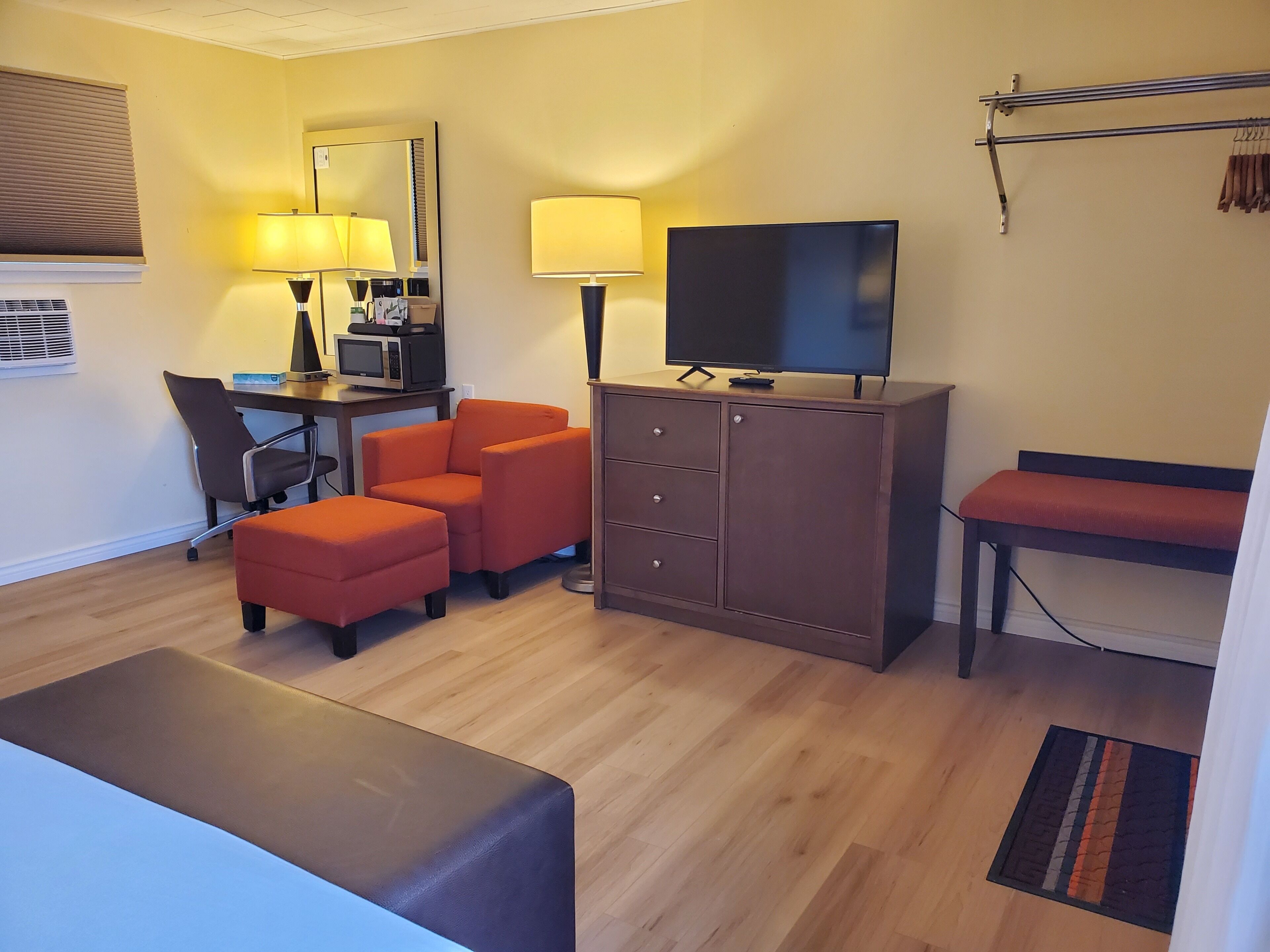 A hotel room with a desk, two chairs, a television, a cabinet, and a bench.