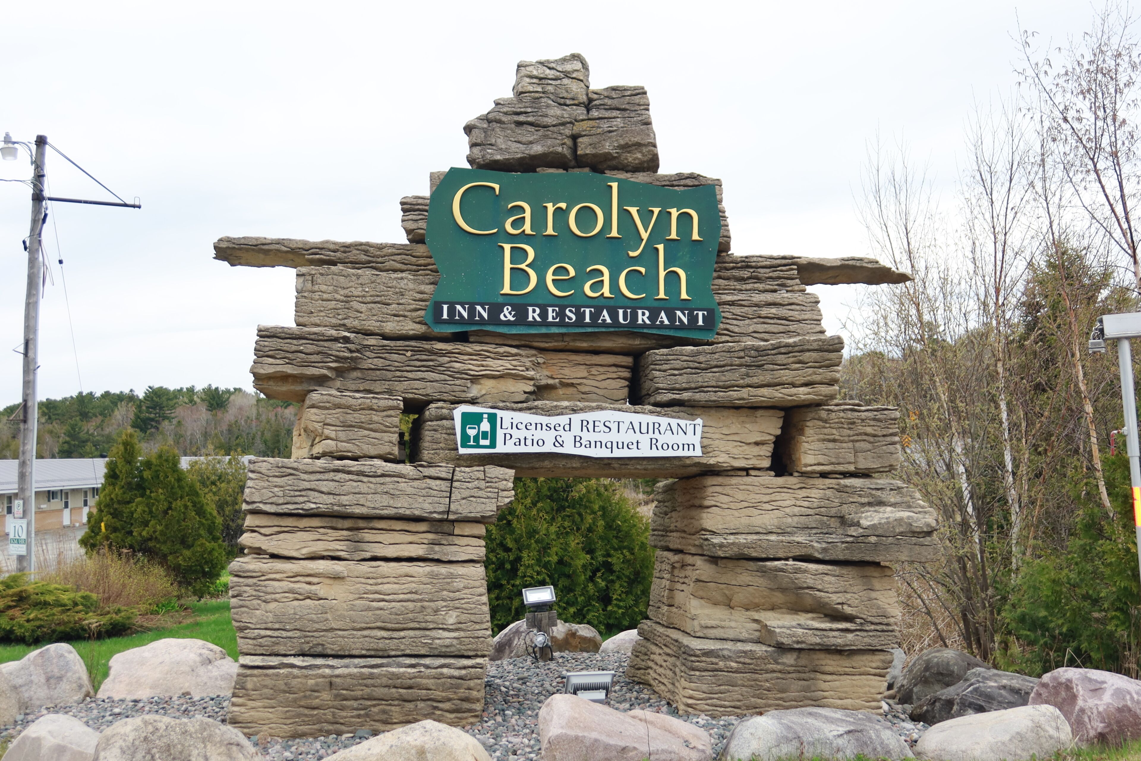 Une arche en pierre surmontée d’une enseigne indiquant le « Carolyn Beach Inn & Restaurant », signalant la présence d’un restaurant agréé et d’une salle de réception.