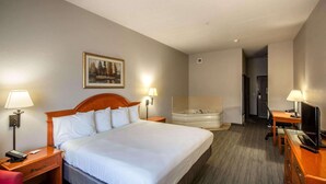 A hotel room with a large bed, a desk with a chair, a desk lamp, a television, a bathroom with a bathtub, and a painting on the wall. - Country Inn & Suites by Radisson, El Dorado, AR (El Dorado)
