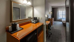A hotel room with a wooden desk, a coffee maker, a microwave, a dresser, a chair, and a large mirror. - Country Inn & Suites by Radisson, El Dorado, AR (El Dorado)