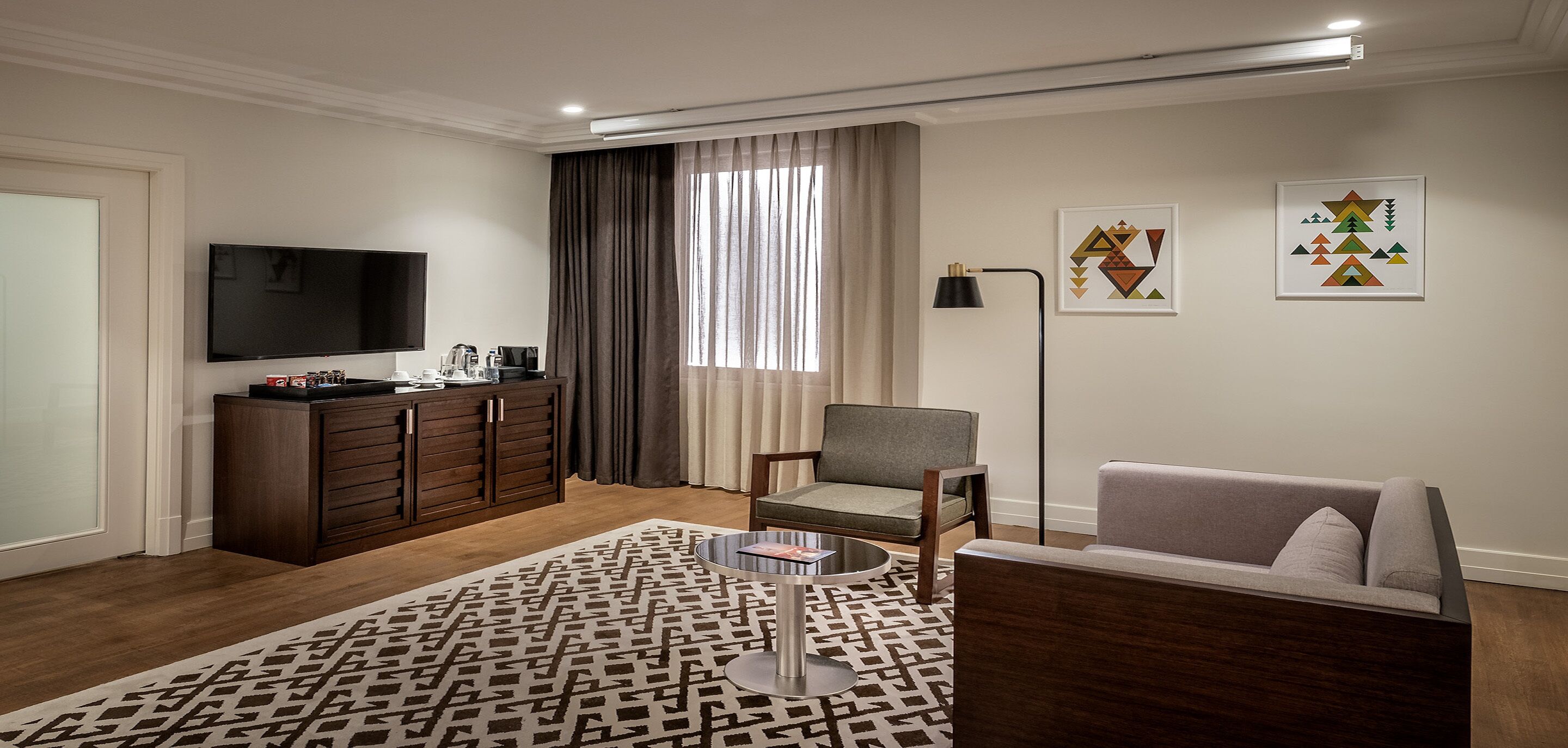 A modern living room with a flat-screen TV, a sofa, a chair, a coffee table, and a patterned rug.