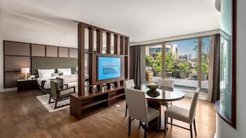 A modern hotel room with a large TV, comfortable seating, a balcony with city views, and a stylish decor.