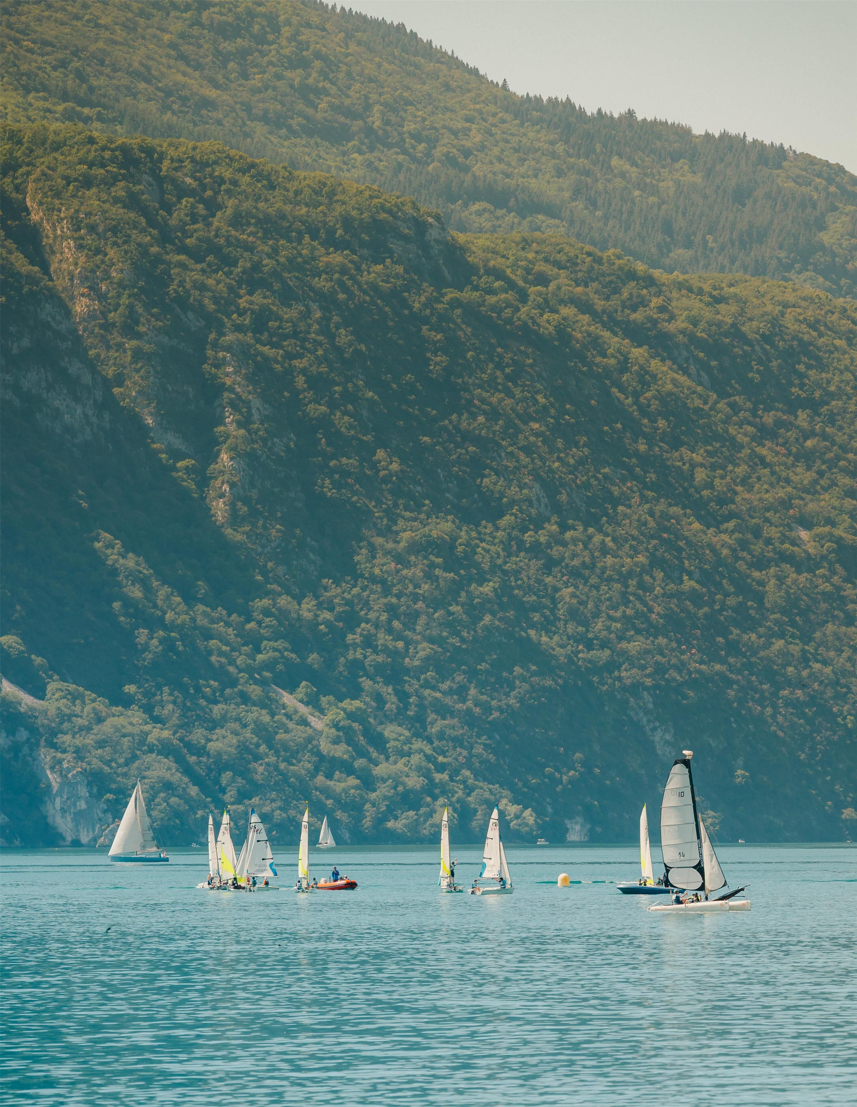 A lake with sailboats and a forested hill in the background.
