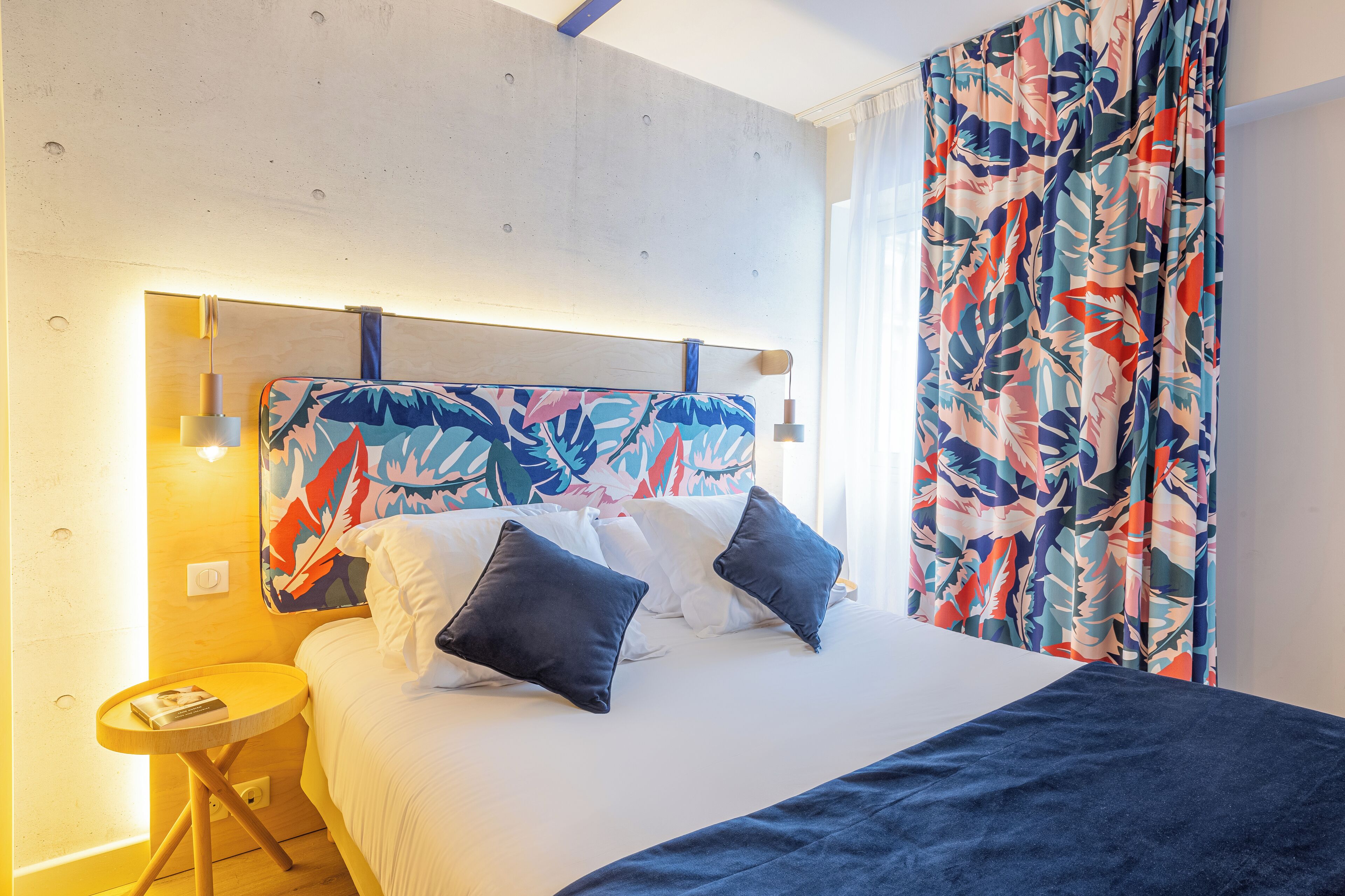 Une chambre à coucher avec un lit, des oreillers, une table de chevet et des rideaux.