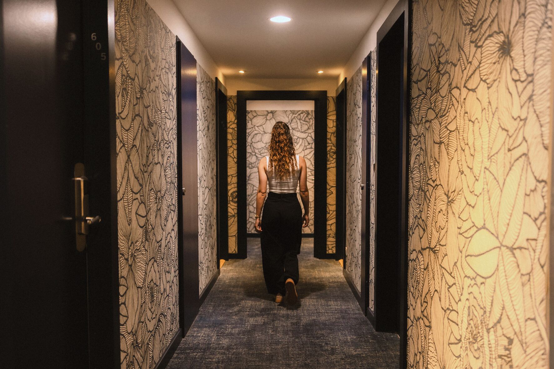 Un couloir avec un papier peint à motifs et une personne qui marche vers une porte.