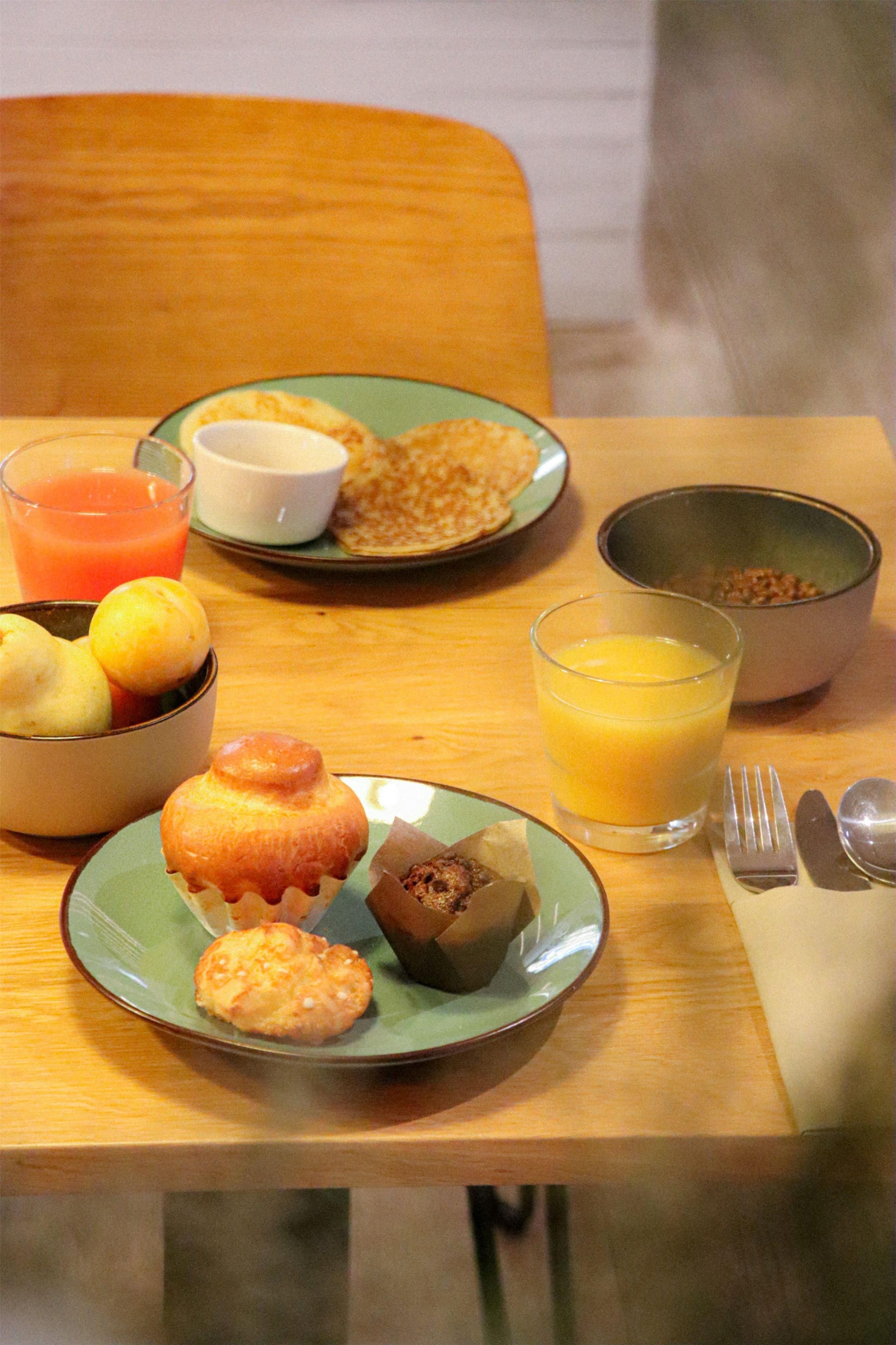 A breakfast setting with plates of food, a bowl of fruit, and glasses of orange juice.