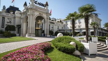 Un bâtiment imposant, doté d’une entrée remarquable, d’une végétation luxuriante et de palmiers.