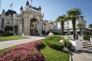Un bâtiment imposant, doté d’une entrée remarquable, d’une végétation luxuriante et de palmiers.