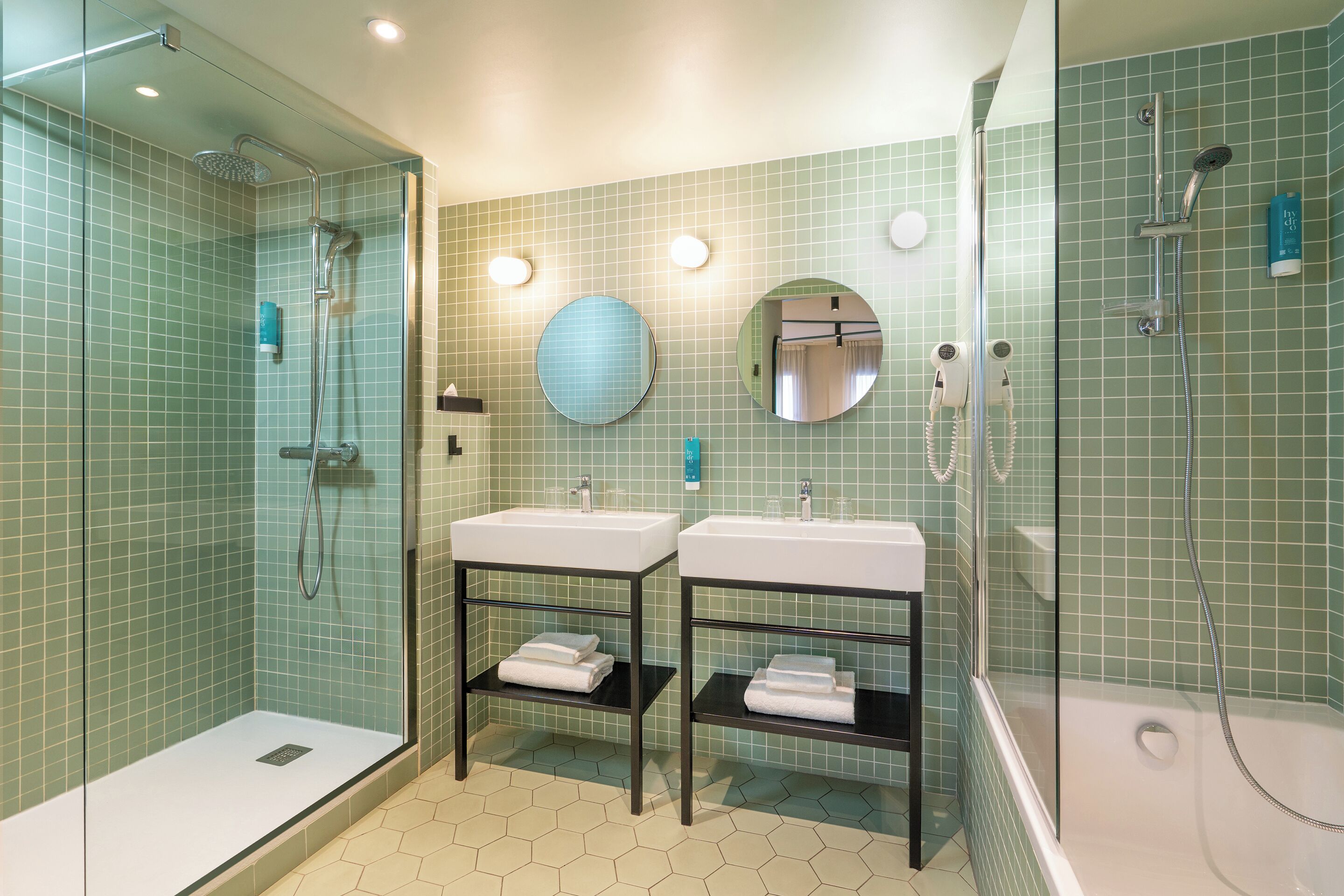 Un baño con dos lavamanos, ducha y zona de ducha con mampara de cristal.