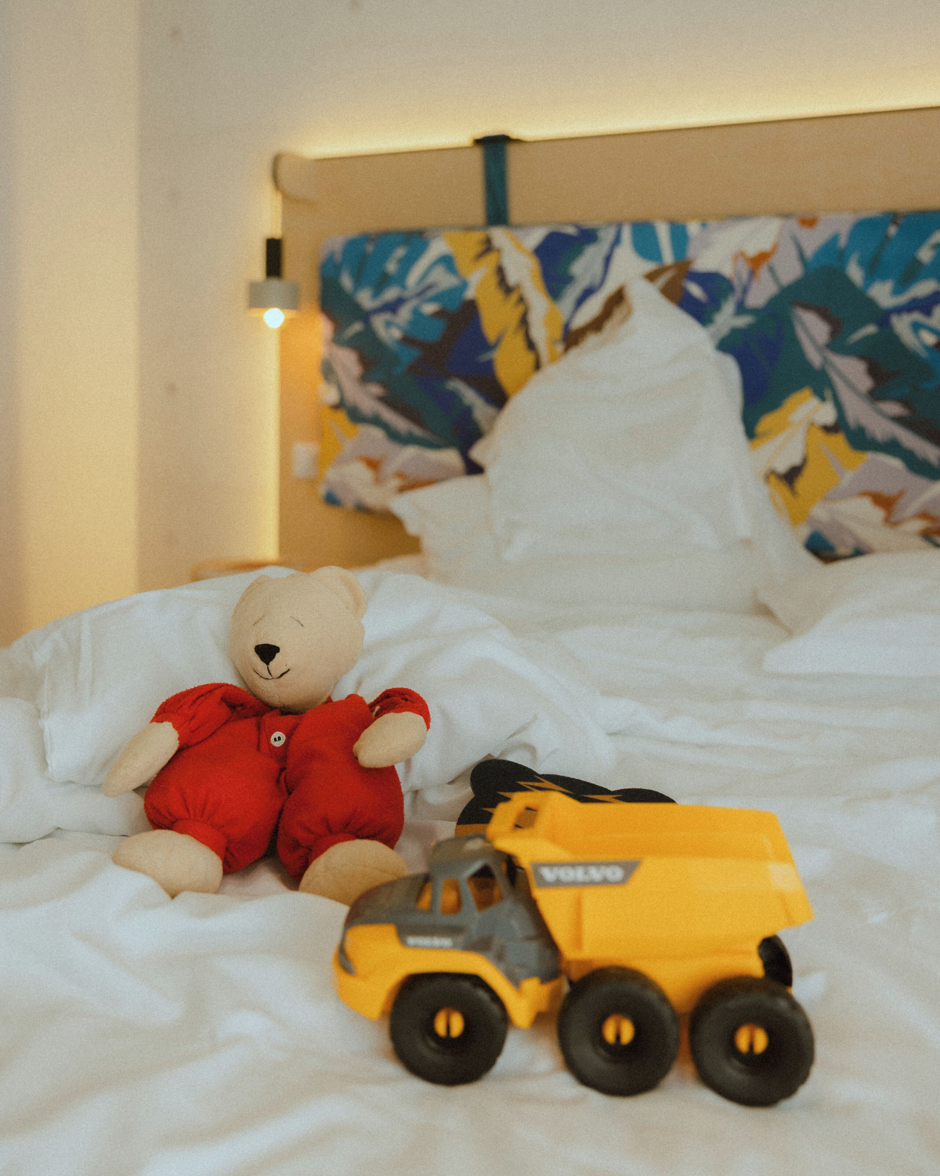 Un lit avec un ours en peluche et un jouet représentant un véhicule.