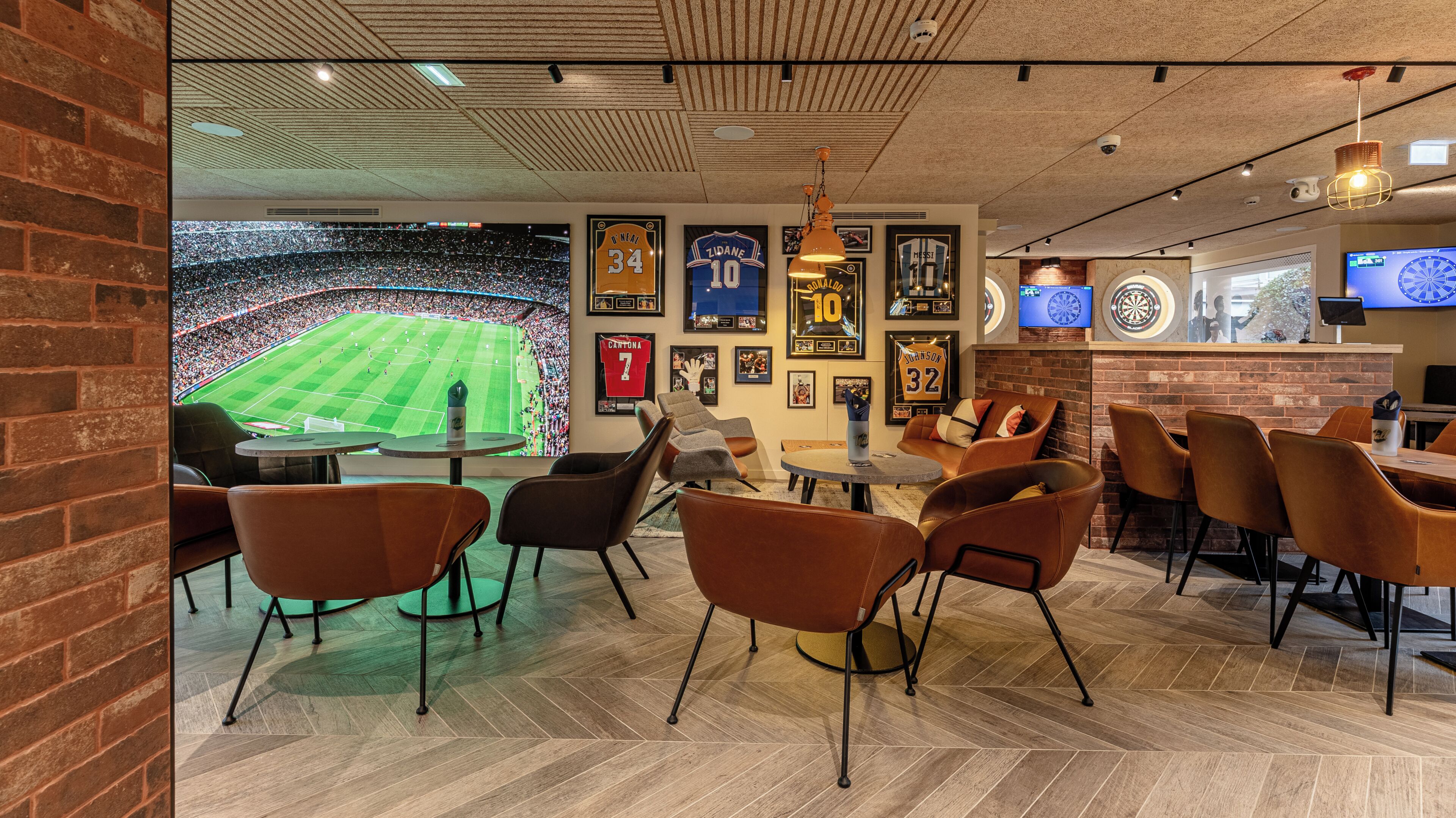 A sports-themed bar with a large TV screen, framed sports memorabilia, and comfortable seating.