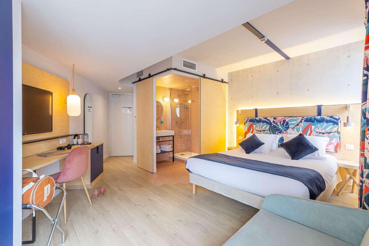 Une chambre d’hôtel moderne équipée d’un lit, d’un bureau, d’une chaise et d’un espace douche.