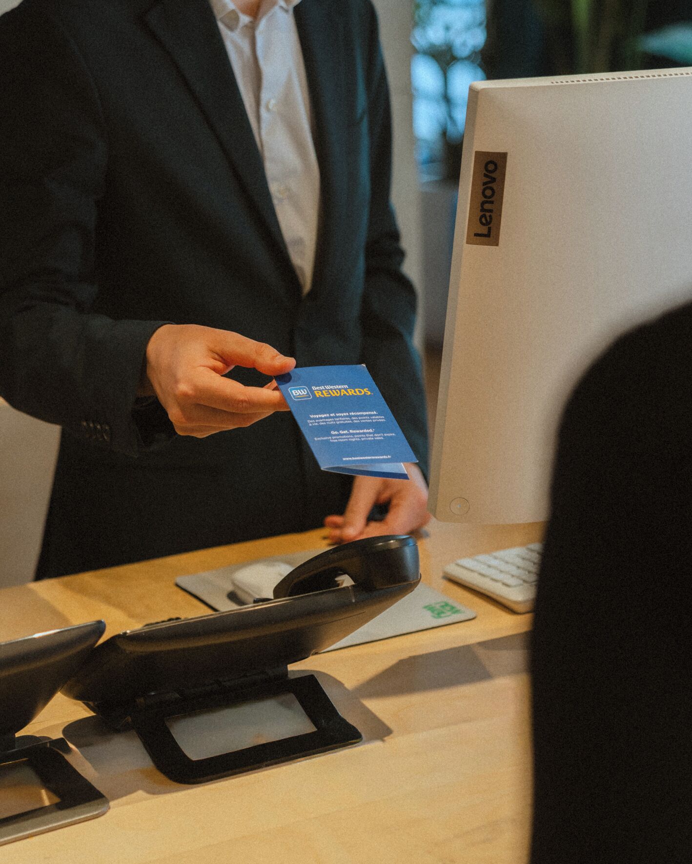 Una persona sostiene una tarjeta azul con texto, de pie frente a una computadora portátil y un teclado sobre un escritorio.