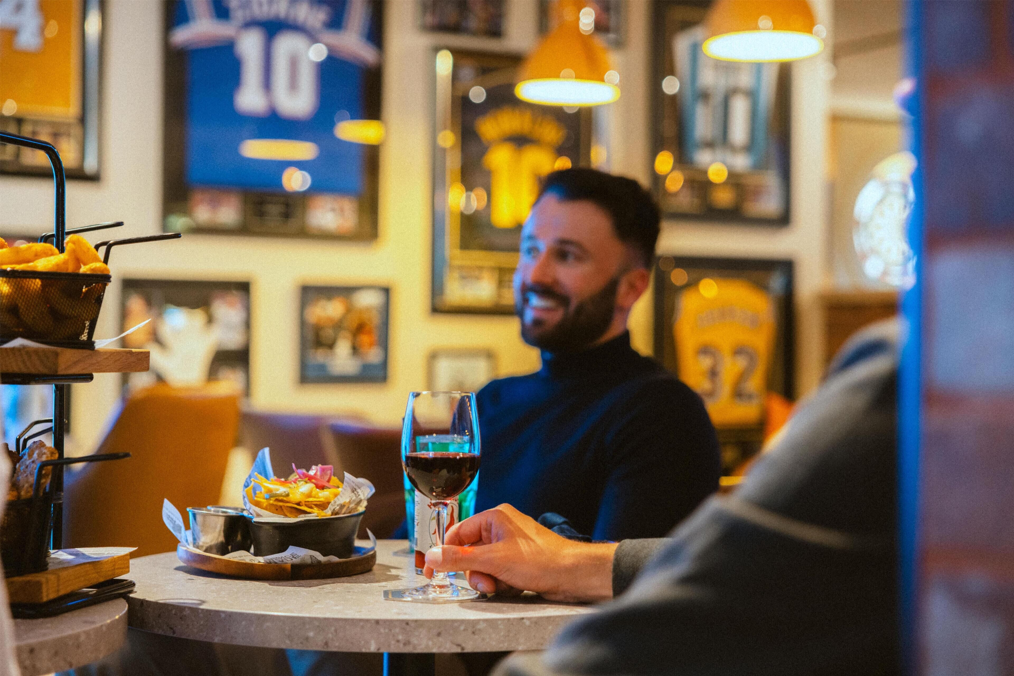 A person seated at a table with a glass of red wine, a basket of fries, and a bowl of salad.