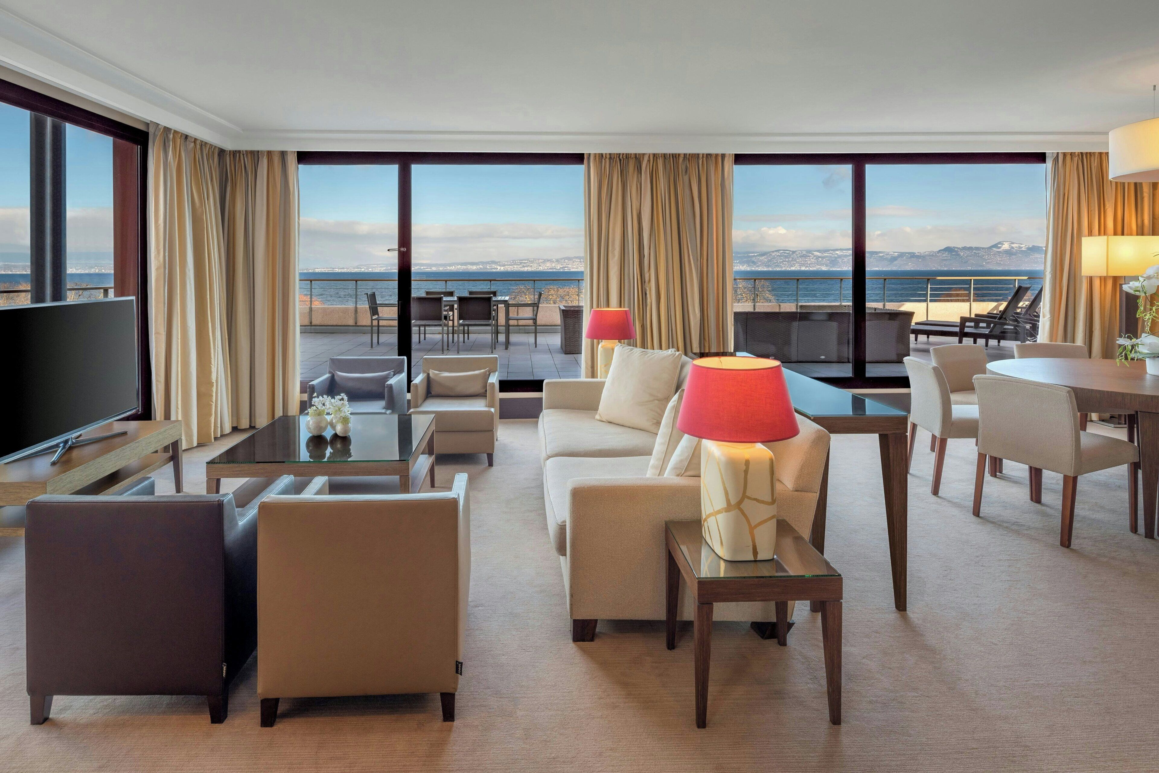 A hotel room with a large TV, seating area, and a view of the sea.